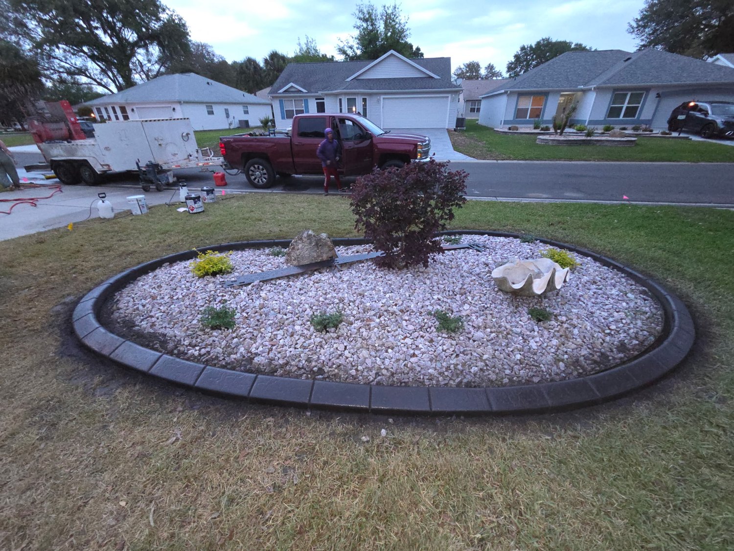 Finished oval landscape bed with dark curved edging and decorative stone