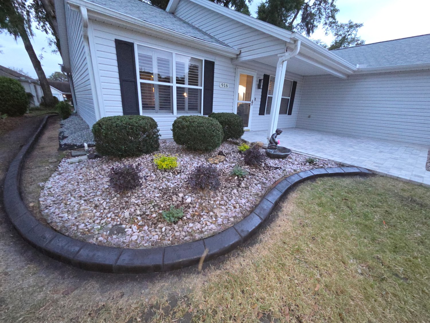 Curved landscape bed with decorative stone and shrubs along the front of a home