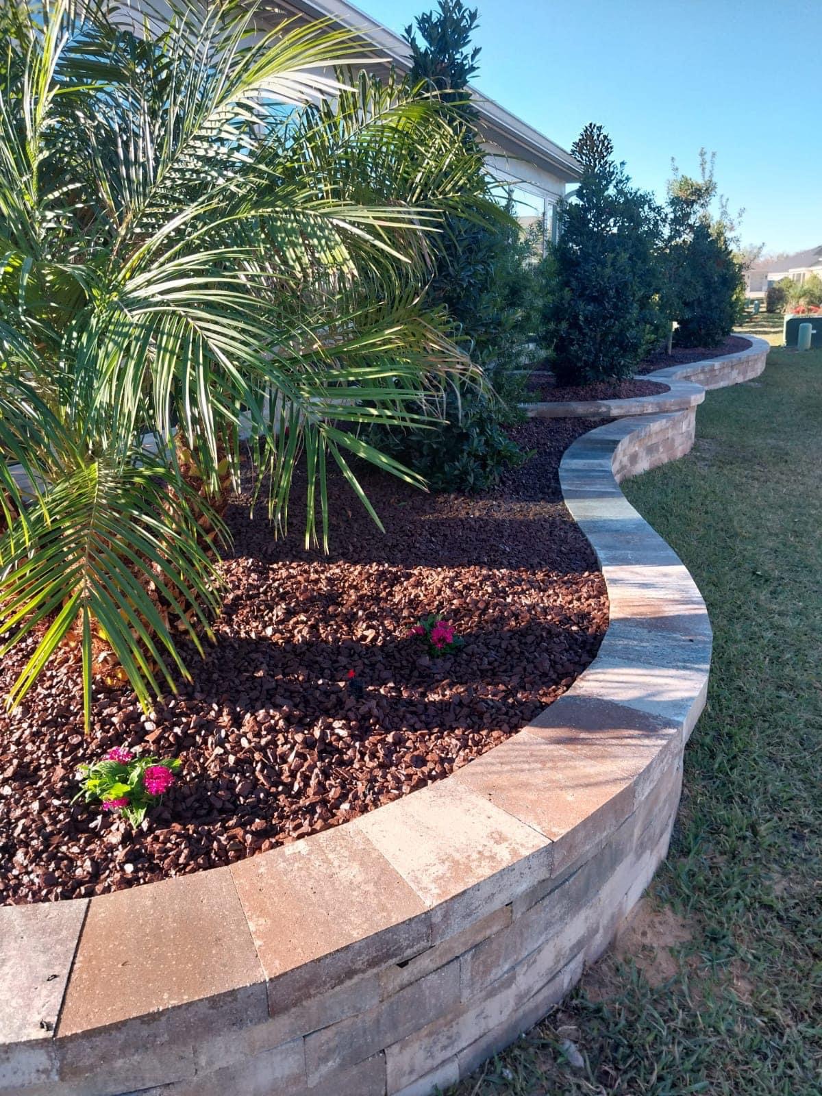 Curved raised landscape retaining wall with capstones and decorative mulch
